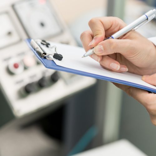 Side view close-up of the hands of a female engineer or inspector, ready for writing a technical report about the manufacturing process in a contemporary factory