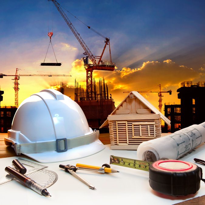 engineer working table plan, home model and writing tool equipment against building construction crane with evening dusky sky